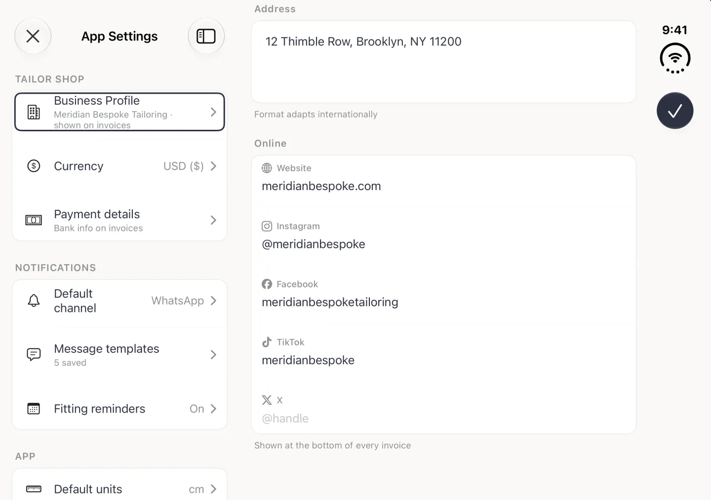 App Settings split view in landscape with Business Profile selected on the left and the Business Profile page on the right scrolled to the end: Address 12 Thimble Row, Brooklyn, NY 11200 with the note Format adapts internationally, then the Online card with Website meridianbespoke.com, Instagram @meridianbespoke, Facebook meridianbespoketailoring, TikTok meridianbespoke and an empty X field with the placeholder @handle, each label beside its platform logo, above the note Shown at the bottom of every invoice; the navy checkmark button sits in the vertical bar strip on the right edge.