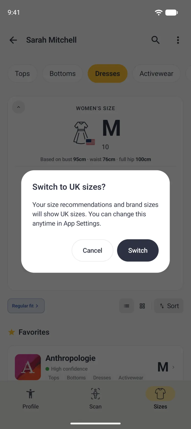 A dialog over the dimmed Sizes tab for Dresses titled Switch to UK sizes? reading Your size recommendations and brand sizes will show UK sizes. You can change this anytime in App Settings., with an outlined Cancel button and a filled navy Switch button.