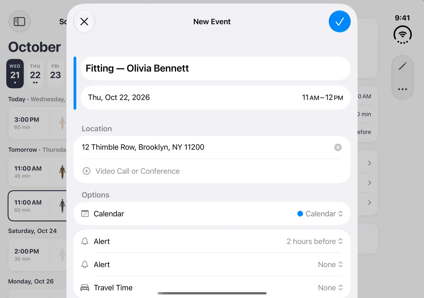 Apple's New Event card centred over the dimmed Schedule split view in landscape, with a close button at the top left and a blue checkmark at the top right. The title reads Fitting, then a dash and Olivia Bennett, the date row reads Thu, Oct 22, 2026 with 11 AM to 12 PM, the location is 12 Thimble Row, Brooklyn, NY 11200, the Calendar row reads Calendar, the first Alert reads 2 hours before, a second Alert None and Travel Time None; the Details further down are out of frame.